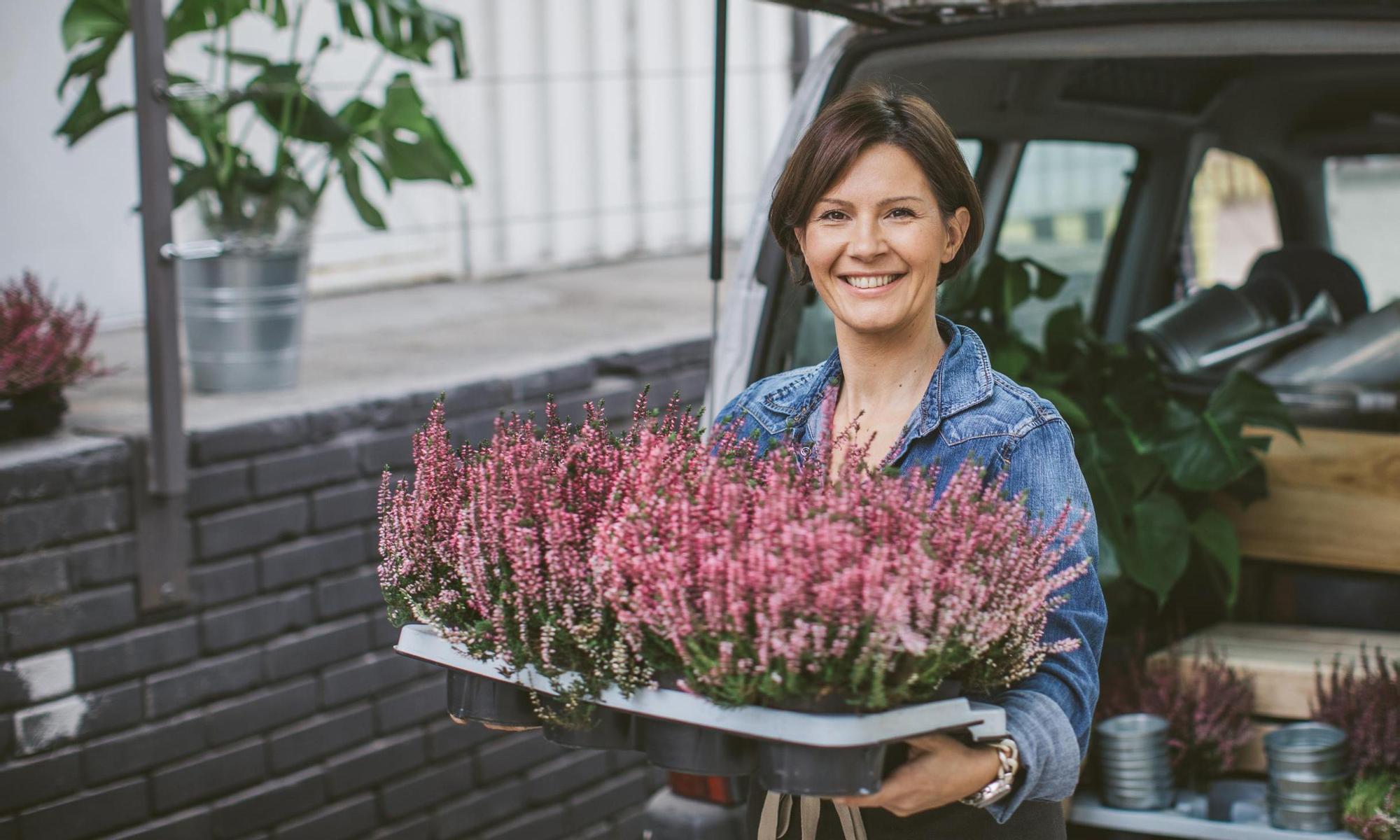 Smiling woman loading car trunk filled with different type of flowers.