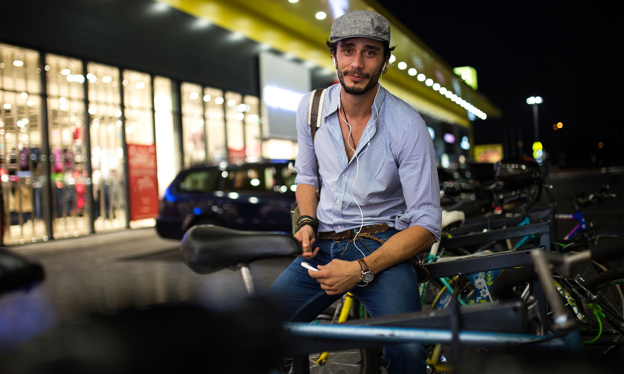 Ung man sitter på ett cykelställ utanför ett köpcentrum på kvällen